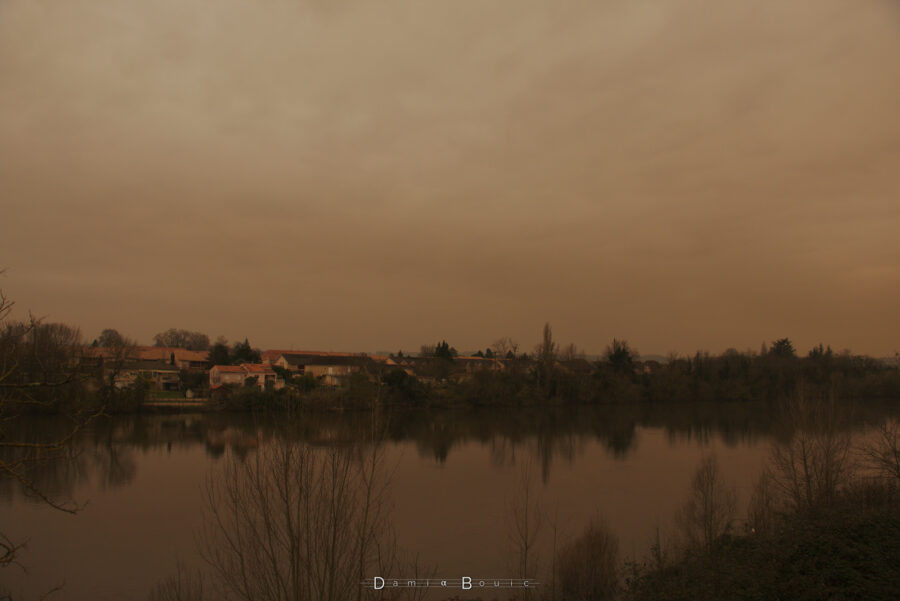 Vue sur le Sud, en plan large, avec la Dordogne et la vue sur la rive opposée, sous un ciel nuageux sombre et ocre