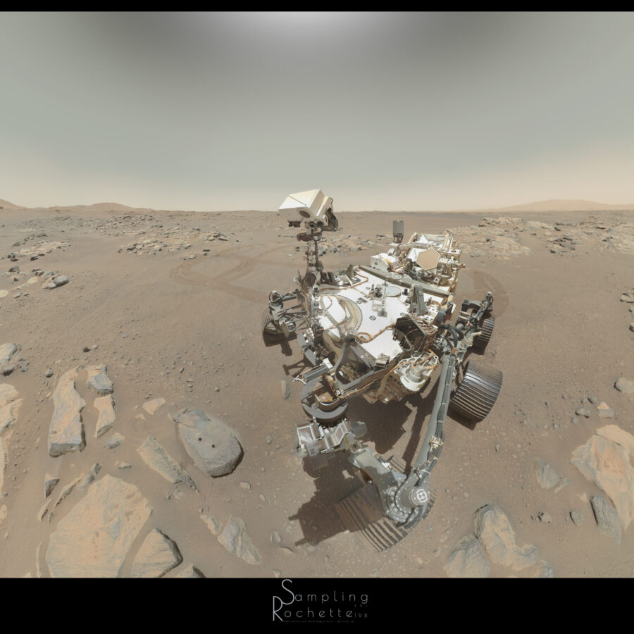 Le rover Perseverance, vu de 3/4, regardant un rocher gris percé de deux trous. D'autres roches entourent le rover, à sa gauche derrière lui les traces de roues témoignent de plusieurs manœuvres. Au loin, horizon légèrement ondulé, et ciel dégagé.