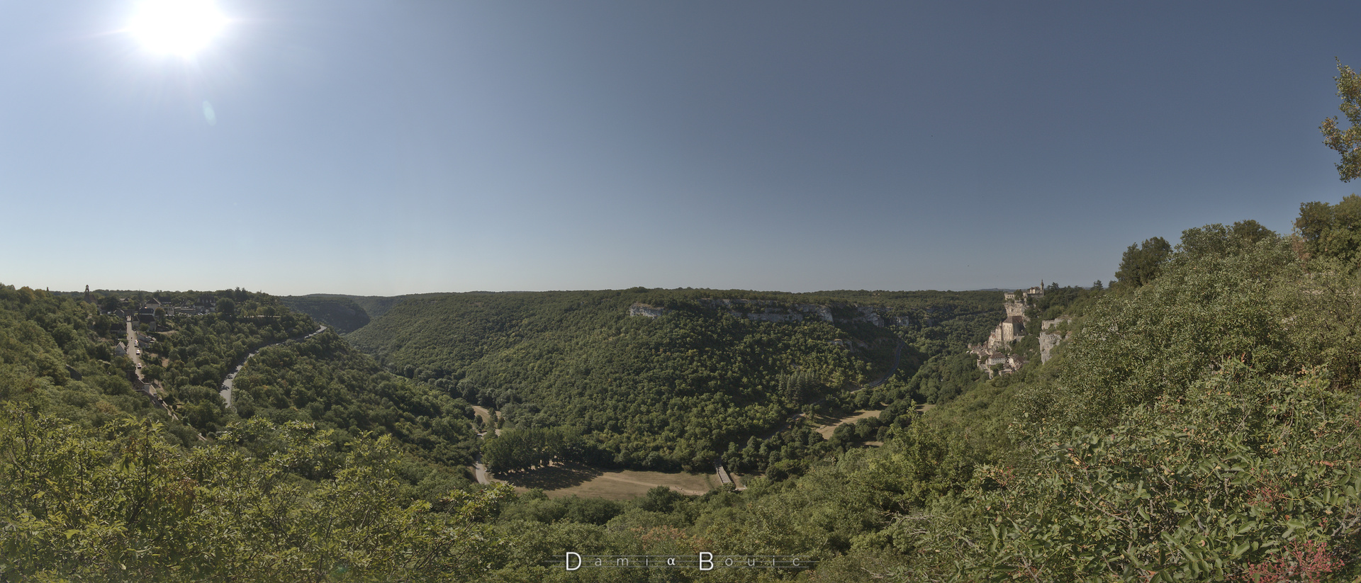 Panorama à 180° sur la vallée, profonde et encaissée, recouverte presque intégralement d'une forêt de feuillus. Quelques rochers émergent vers le milieu en haut. A droite toute, la cité de Rocamadour, accrochée à sa falaise éternelle et sacrée