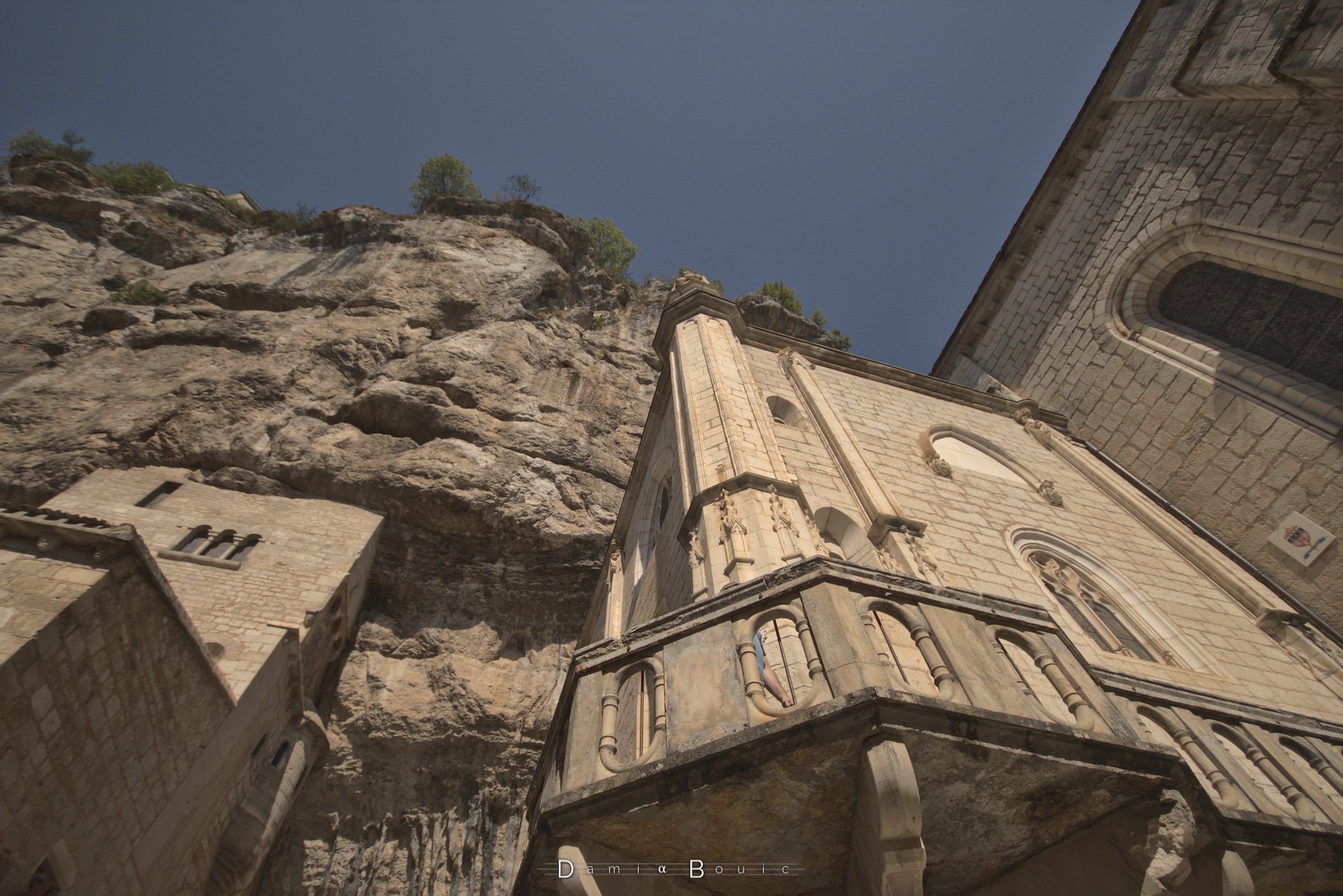 Contre plongée sur un mur d'église, dont une partie et flanquée dans la falaise calcaire qui domine la scène. 