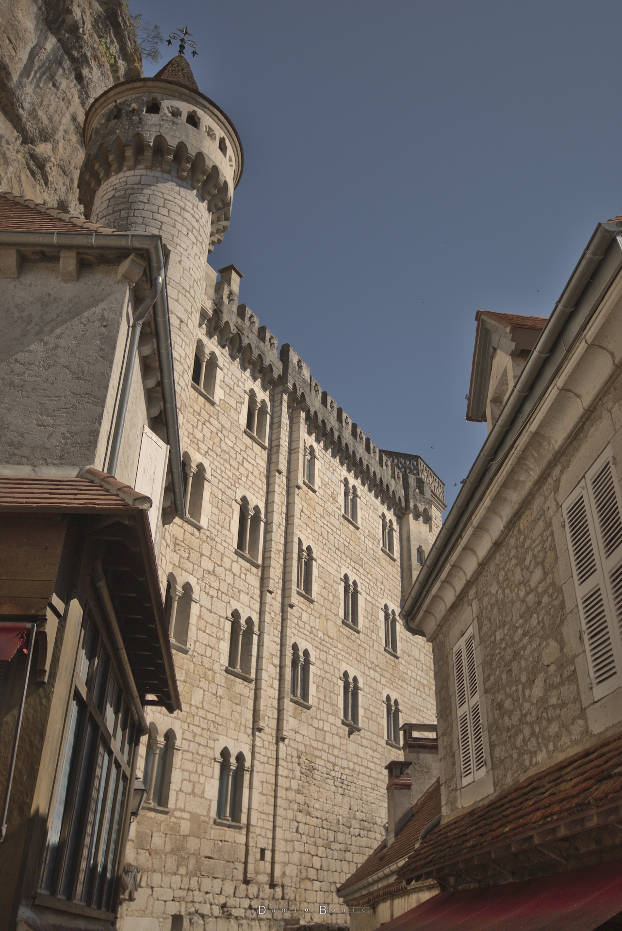 Vue sur le même édifice, mais d'en bas, en légère contre plongée. L'aspect médiéval de cette architecture religieuse ressort bien avec la tourelle bien cylindrique, qui termine un mur aux fenêtre petites, et au sommet garni de créneaux et de machicoulis.