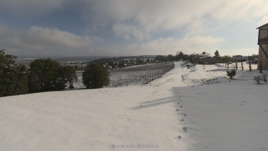 Paysage valloné blanchi par la neige, à peine dérangée par quelques traces de pas. Ciel bleu avec quelques nuages. 