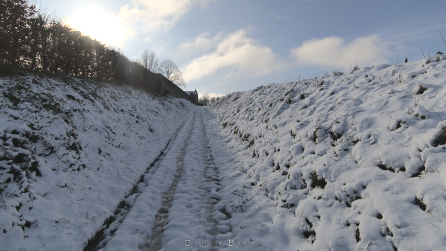 Chemin de terre encaissé couvert de neige, débordant l'horizon de toutes parts.