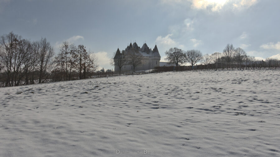 Le château de Monbazillac au milieu d'un champs enneigé, partiellement caché par quelques arbres décharnés.