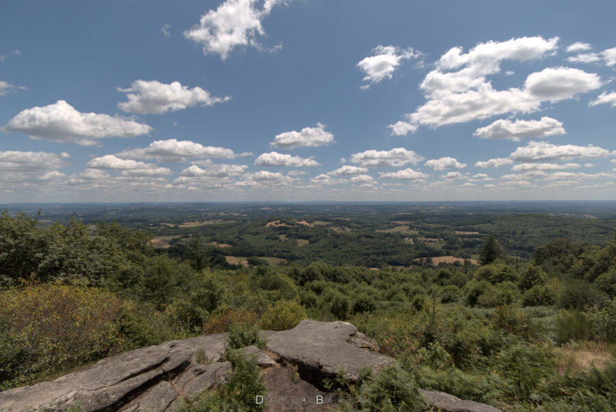 Près du sommet, sur des rochers de granites, la vue porte très loin et montre un paysage varié de forêts, de bosquets et autres clairières. L'horizon qui s'enfonce dans la brume ondule doucement, sous un ciel ponctué de cumulus dans un fond bleu roi et un Soleil insolent 