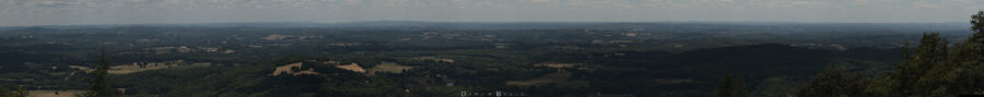 Panorama très serré sur l'horizon, offrant une vue extrêmement détaillée ce qu'y s'y trouve, avec des collines multiples, beaucoup de végétation, forêts, clairière, et maison diverses, toutes petites, telles des maquettes dans un diorama