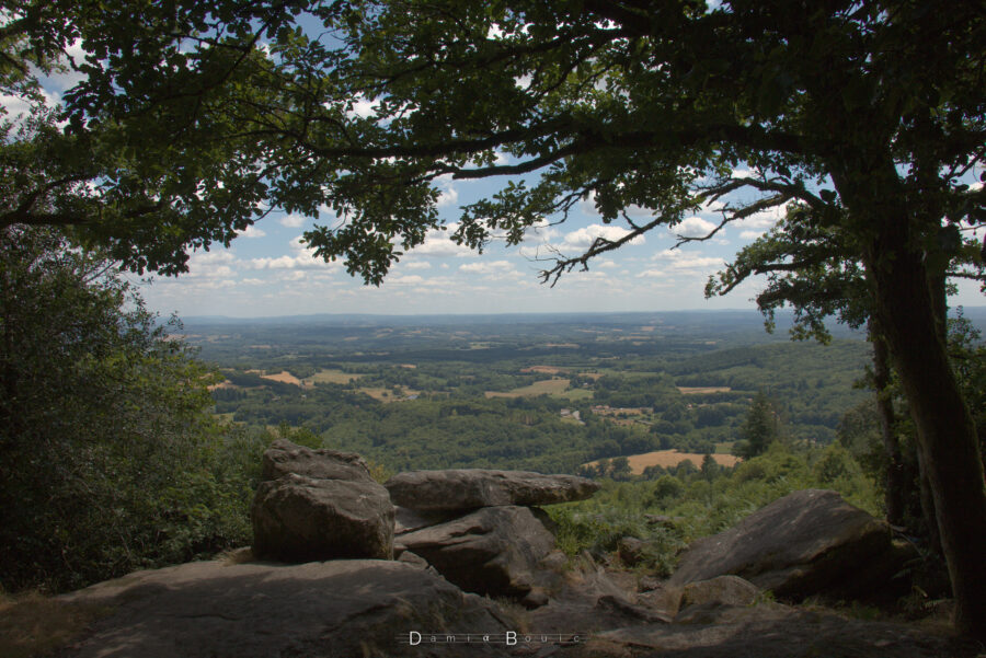 Des branches et un tronc d'arbre font office de cadre pour cette photo montrant le paysage et sa vue impressionnant. Des rochers granitiques achèvent de former ce cadre en bas de la photo