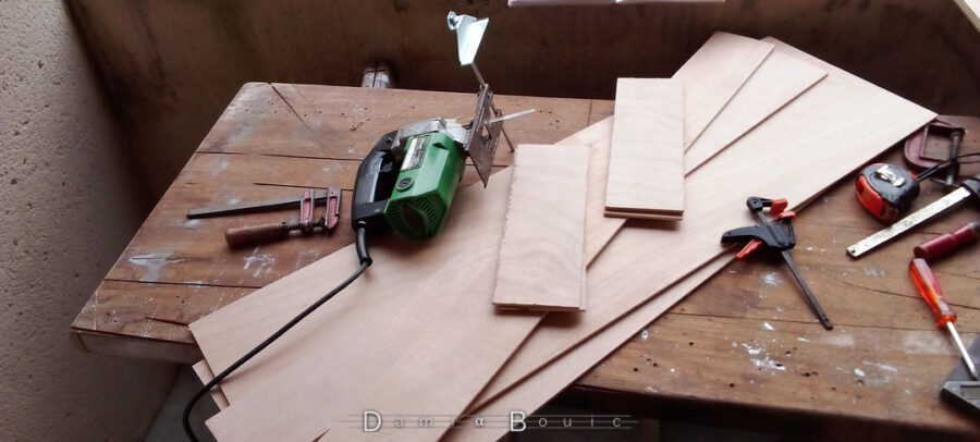 Sur l'établi. Planches de contreplaqué fin (4mm). Deux grandes planches, deux plus étoites, et deux plus petites. La scie sauteuse qui a permis ce travail reposé à côté, lame en l'air, à côté d'un serre-joint