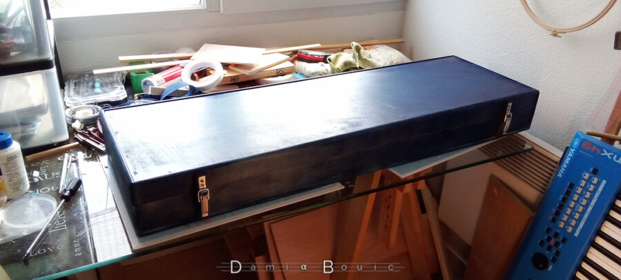 L'étui désormais assemblé, est peint, et repose sur la table de l'atelier intérieur.