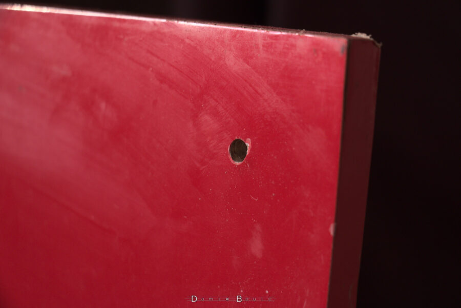 Détail sur un coin de la planche rouge montrant un trou impeccable pratiqué dans un angle.