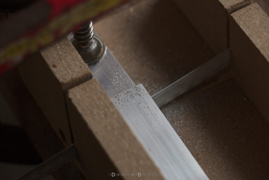 Détail sur l'une des nombreuses coupes à la scie à métaux manuelle montrant l'aluminium coupé en deux, avec un peu de poudre métallique autour