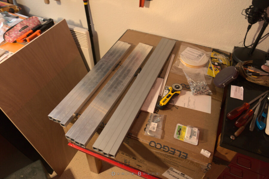 A l'intérieur, je regroupe par 3 groupes de longueurs les poutrelles. A gauche on peut voir la planche en contreplaqué qui servira de porte. Sous les poutrelles, la grosse boite en carton qui contient l'imprimante 3D, marquée du logo d'Elegoo