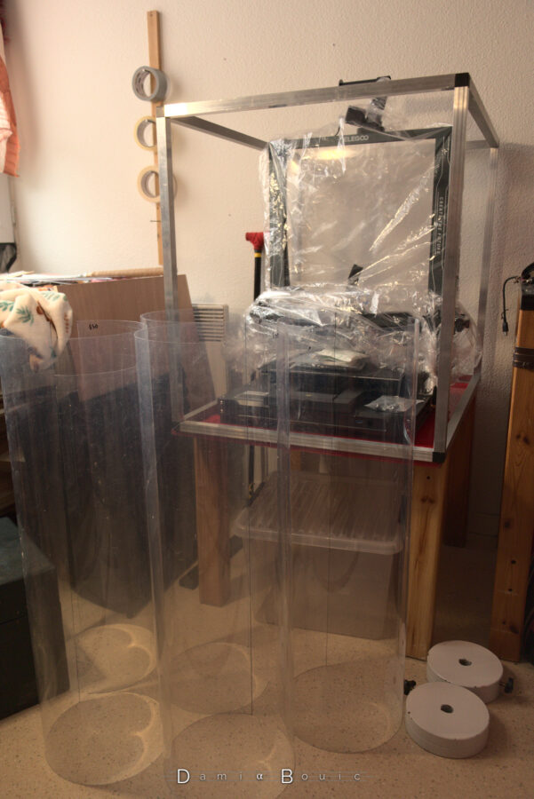 Devant le squelette rectangulaire cubique du futur caisson, les différentes feuilles de plastique transparent reposent verticalement car elles s'enroulent naturellement en cylindres.