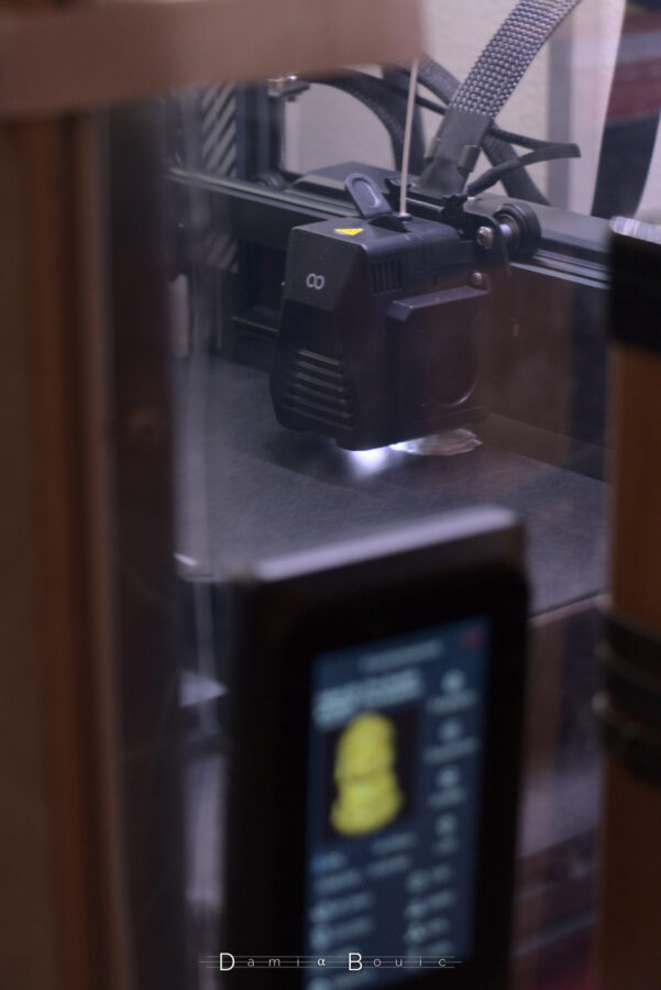 Derrière une raquette de commande floue car la mise au point n'est pas faite dessu, la buse de l'imprimante qui commence son travail, avec une petite forme aux contours ronds. Ça ressemble à chewing-gum.