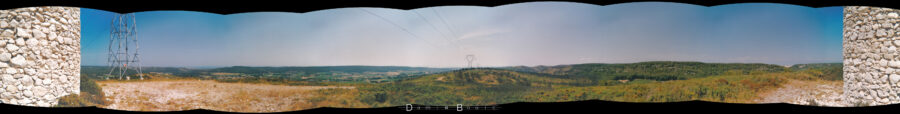 Panorama complet sur 360°, de plusieurs photos assemblées entre elles, qui montre un paysage de garrigue typique, la méditerranée en fond quand celle-ci n'est pas cachée par quelques collines de pins. Le Soleil est écrasant, les couleurs sont vives, on pourrait presque sentir la chaleur de cette journée d'été. Quelques lignes électriques de THT hantent le site jusqu'à l'horizon. 