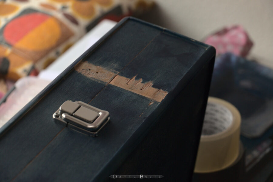 Vue à peu près identique, sauf que cette fois-ci le loquet fait face au ciel. Les pièces de bois servant de support aux anciens loquets ont été enlevées, révélant une zone de bois non peinte plus large. Les trous qui servent de passage aux vis sont visibles dans ces zones, qui ont été par ailleurs poncées pour les préparer à la peinture.