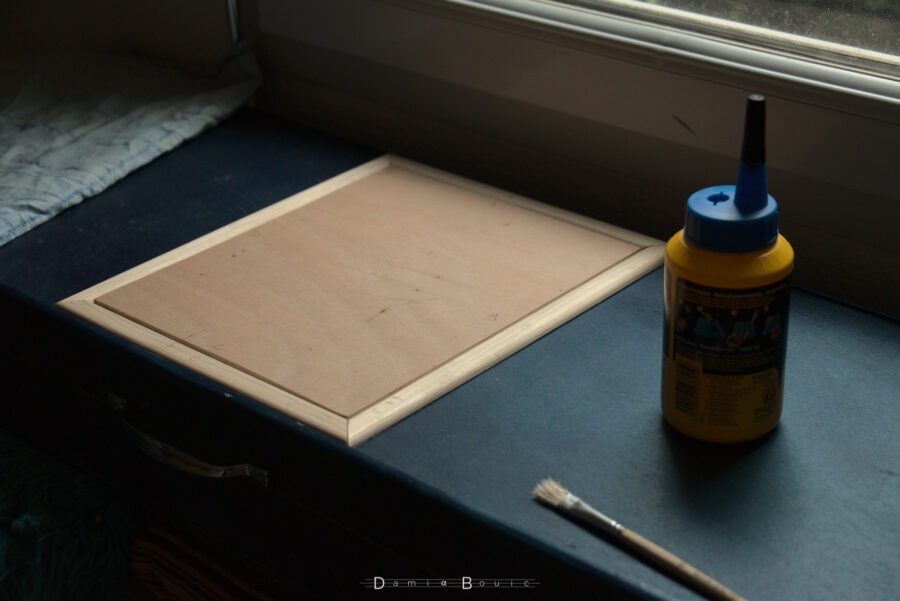 La même scène, sans le papier imprimé, avec le pot de colle à bois et un pinceau plat. Tout est prêt à être collé, sauf la plaque centrale.