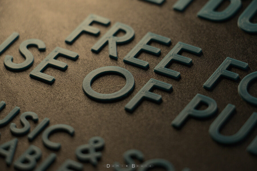 Zoom sur la partie centrale des lettres, qui brillent sous une lumière tamisée, révélant le tracé de l'impression filaire dans les lettres