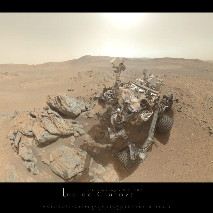 Vue large sur un paysage martien, dont l'horizon est parcouru de nombreuses collines, avec la vue qui porte assez loin par endroits, surtout à droite. Toute la partie droite est occupée par le rover Perseverance, gros engin à plusieurs roues, recouvert de poussière par endroit, dont les caméras situées sur un mât observent un groupe de gros rochers juste à gauche, certains ayant reçu des marques de polissage circulaire. C'est le milieu de la journée, le Soleil illumine fortement la scène par le zénith.