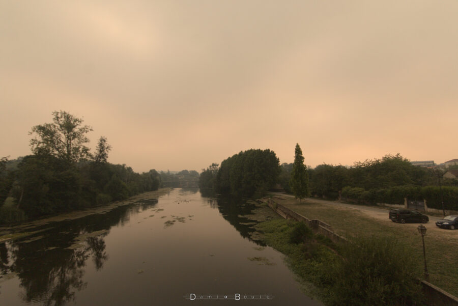 Vue sur la rivière de l'Isle, dont le niveau très bas est trahit par les rives à sec. Le ciel est chargé et jaunâtre