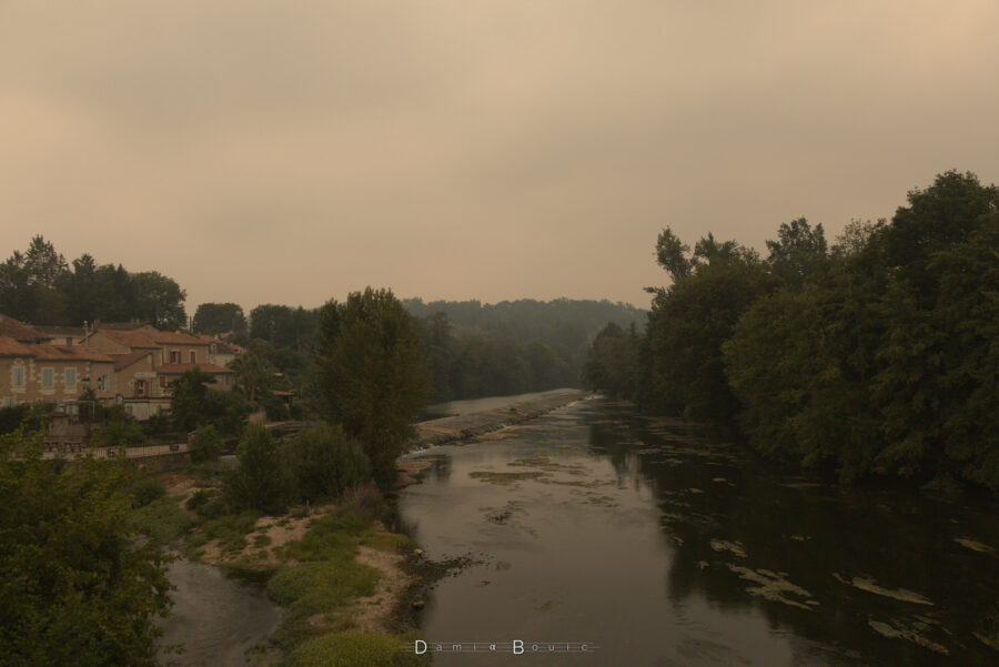 Autre vue sur l'Isle, au niveau très bas donc. Un barrage est surmonté d'une fine pellicule d'eau qui indique bien un faible débit des eaux. Beaucoup d'arbres à gauche et une forêt au fond au milieu perdue dans les brumes de pollution.