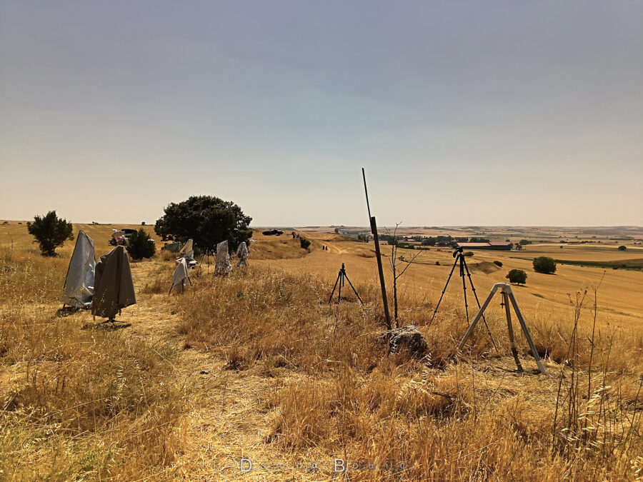 Dans un paysage d'herbes grillées par le Soleil, avec une vue sur la plaine, de nombreux trépieds sont disposés, comme autant de petits arbres, certains coiffés de tissus et autres bâches de protection contre le Soleil.