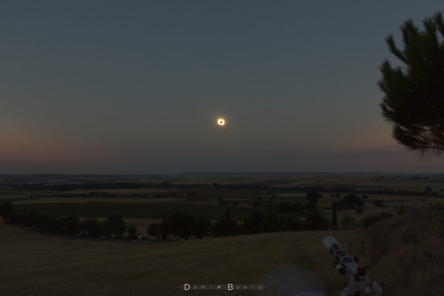 Le paysage sous l'éclipse totale de Soleil, visible au milieu avec un point noir entouré d'un anneau brillant. Sur l'horizon et de part et d'autre, des zones de ciel encore dans la lumière du jour