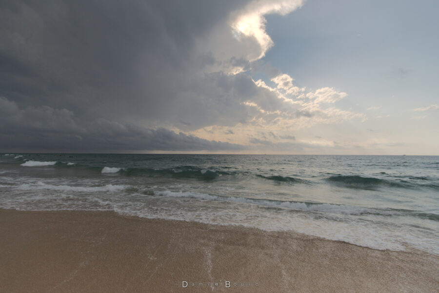 Toujours depuis le bord de l'eau sur la plage, le cumulonimbus recouvre le Soleil, assombrissant la scène. Le ciel devient menaçant.